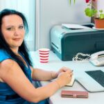 Brunetka w biurze domowym pracuje na laptopie, patrząc na fotoaparatu.