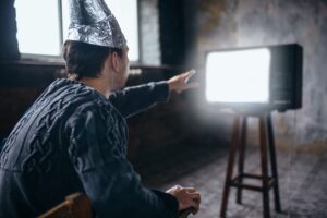 Mężczyzna w kasku z folii aluminiowej sięga do telewizora