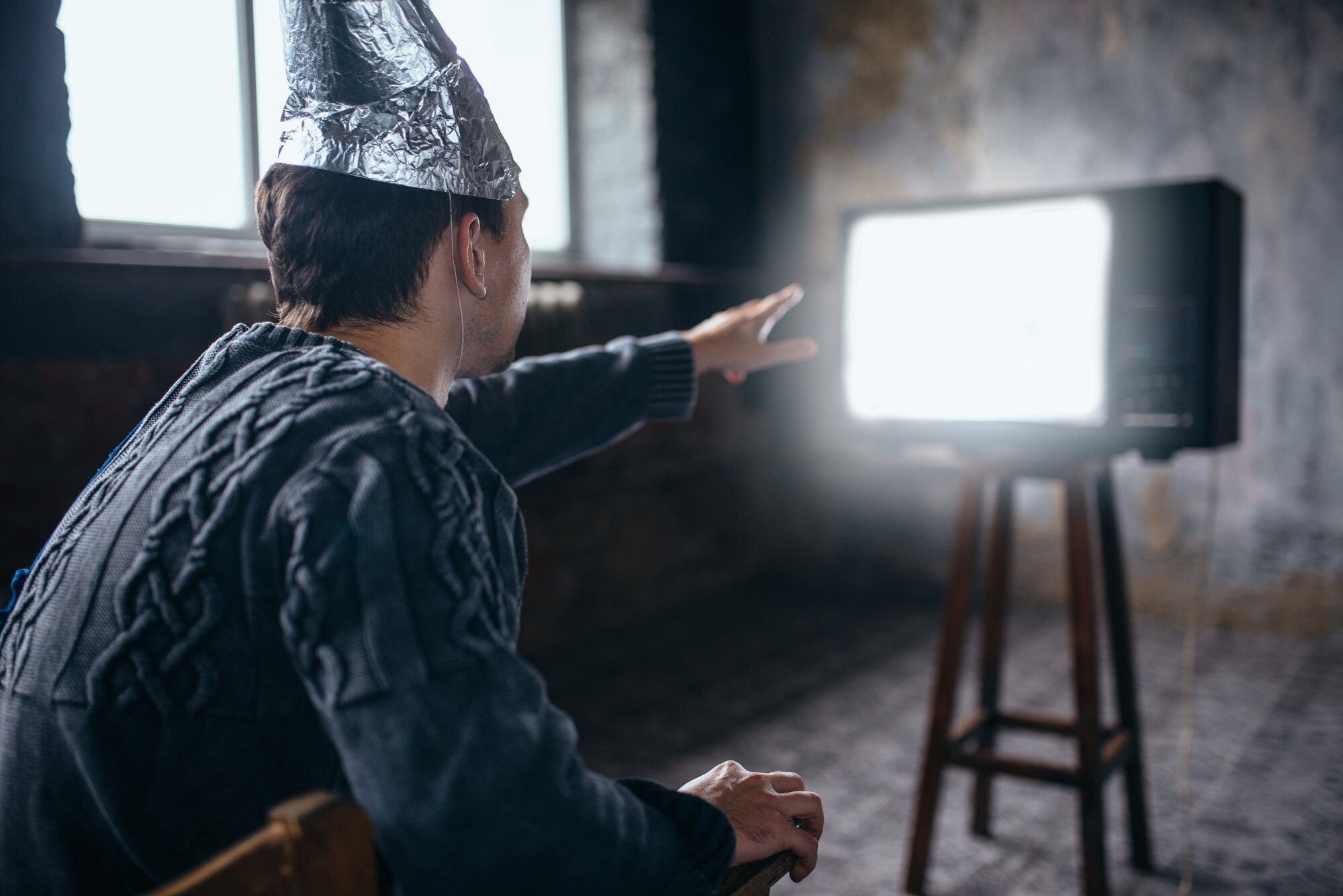 Mężczyzna w kasku z folii aluminiowej sięga do telewizora
