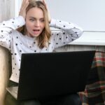 Młoda kobieta siedząca na balkonie obok laptopa krzycząc stres online edukacja zostań w domu koncepcja
