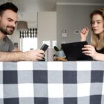 Mężczyzna i kobieta używający sprzętu technologicznego na stole jadalnym w domu
