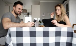 Mężczyzna i kobieta używający sprzętu technologicznego na stole jadalnym w domu