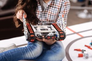 Ciesz się klasą techniczną. Zaangażowano utalentowaną małą dziewczynkę siedzącą w laboratorium robotyki i trzymającą szczegóły cyber robota podczas zajęć technicznych