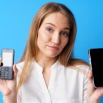 Młoda kobieta trzyma stary i nowy telefon na niebieskim tle