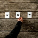 Wysoki kąt widzenia web developera umieszczającego trzy białe księgi pisowni WWW na teksturowanych rustykalnych drewnianych deskach. Koncepcyjne profesjonalistów internetowych w Internecie.