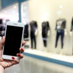 kobieta trzyma smartfon stoi przed centrum handlowym.