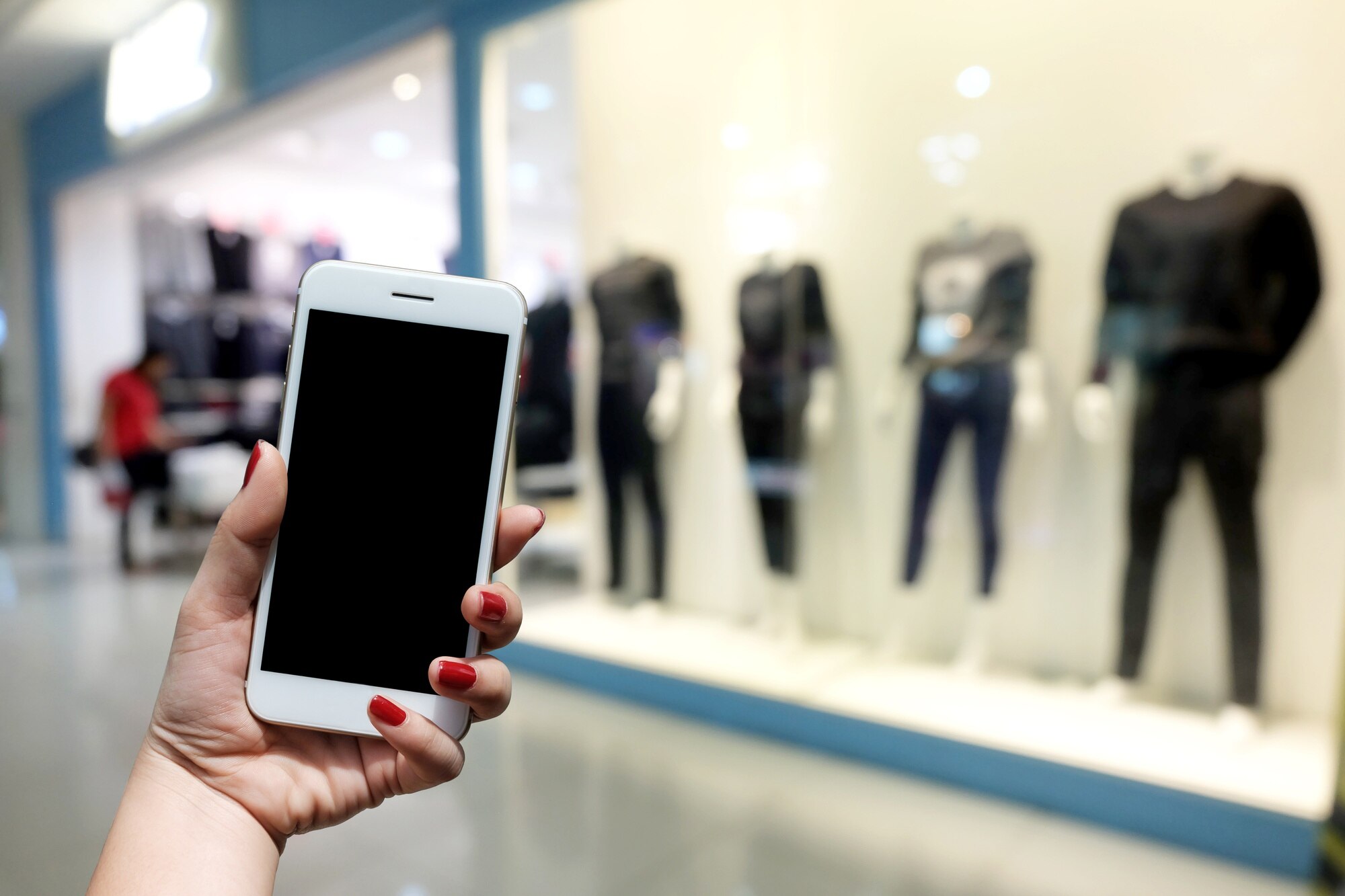 kobieta trzyma smartfon stoi przed centrum handlowym.