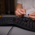 W zbliżeniu widać rękę używającą narzędzia wyciągającego klawisze do skrupulatnego usunięcia klawisza klawiatury