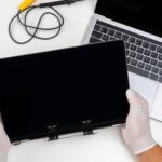 Mężczyzna wymienił zepsuty monitor na laptopie i trzyma go w dłoniach w jasnym białym pokoju