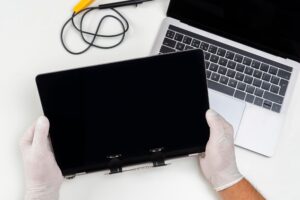 Mężczyzna wymienił zepsuty monitor na laptopie i trzyma go w dłoniach w jasnym białym pokoju