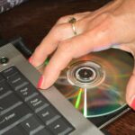 Ręka kobiety biorąca płytę DVD z laptopa