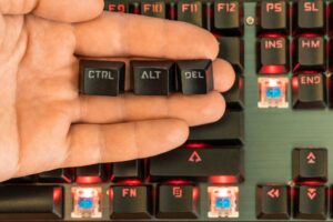 męska ręka trzyma na dłoni trzy klawisze - ctrl alt del nad czarną podświetlaną klawiaturą