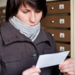 Dziewczyna w płaszczu uważnie patrząca na konto otrzymane pocztą