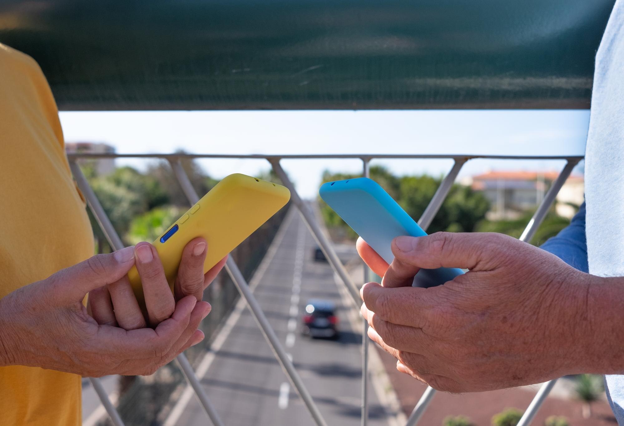Kilka osób trzyma telefon komórkowy w pokrowcach dopasowanych do ubrania Stojąc na moście nad ruchem miejskim