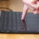 Osoba naciska przyciski na klawiaturze laptopa dwoma palcami