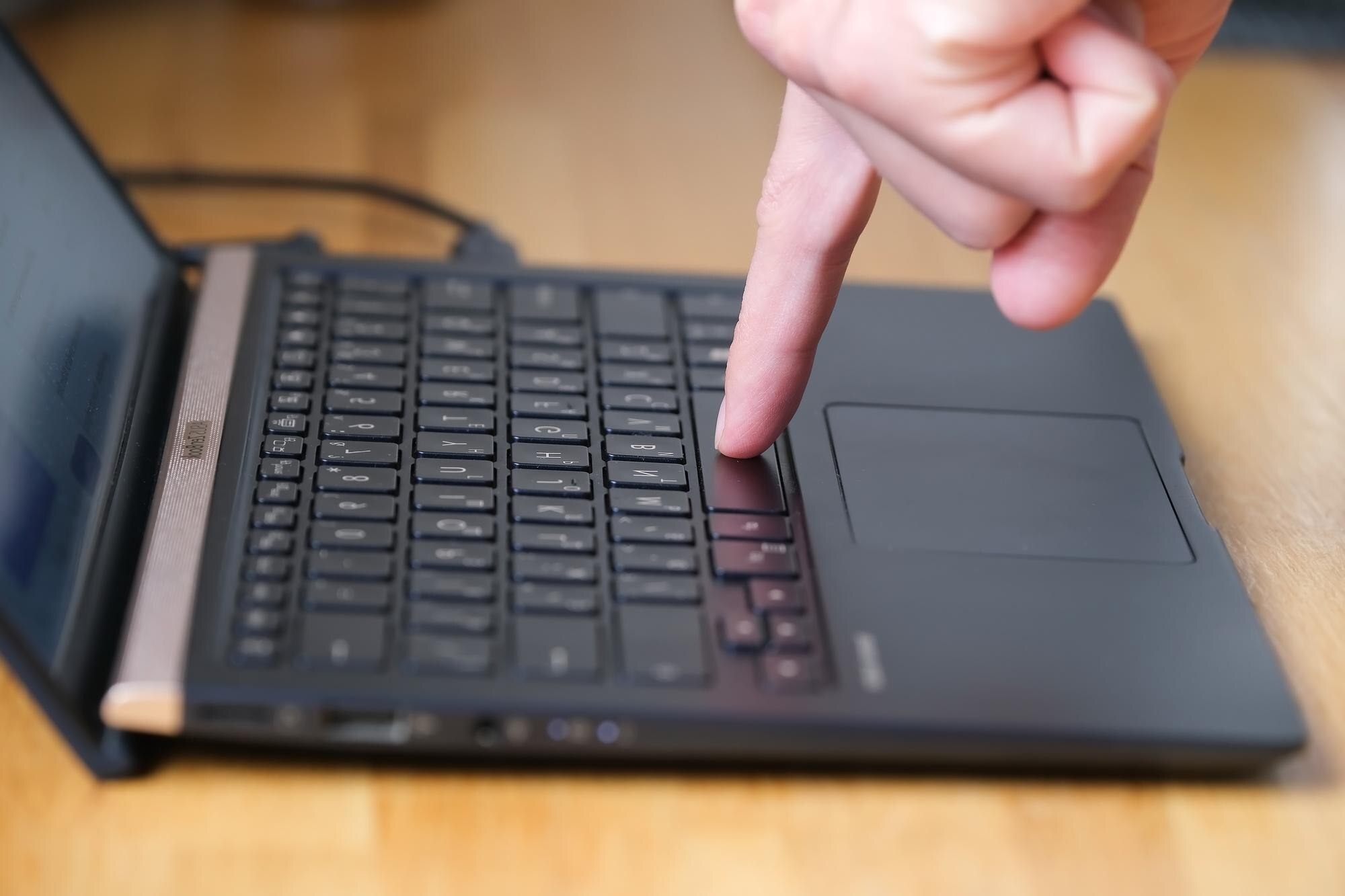 Osoba naciska przyciski na klawiaturze laptopa dwoma palcami
