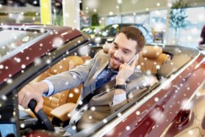 biznes samochodowy, sprzedaż samochodów, konsumpcjonizm, technologia i koncepcja ludzi - szczęśliwy człowiek siedzący w samochodzie i dzwoniący na smartfonie na pokazie samochodowym lub salonie nad efektem śniegu