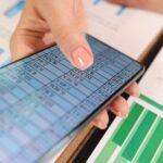 Zbliżenie dłoni kobiety biznesu z danymi finansowymi na ekranie smartfona i stole biurowym z dokumentami