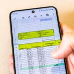 Mężczyzna przewracający arkusz Excel na ekranie telefonu pokazujący tabelę amortyzacji kredytów bankowych