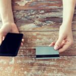koncepcja biznesu, technologii, gotówki i Internetu - zbliżenie męskich rąk trzymających inteligentny telefon i kartę kredytową na drewnianym stole