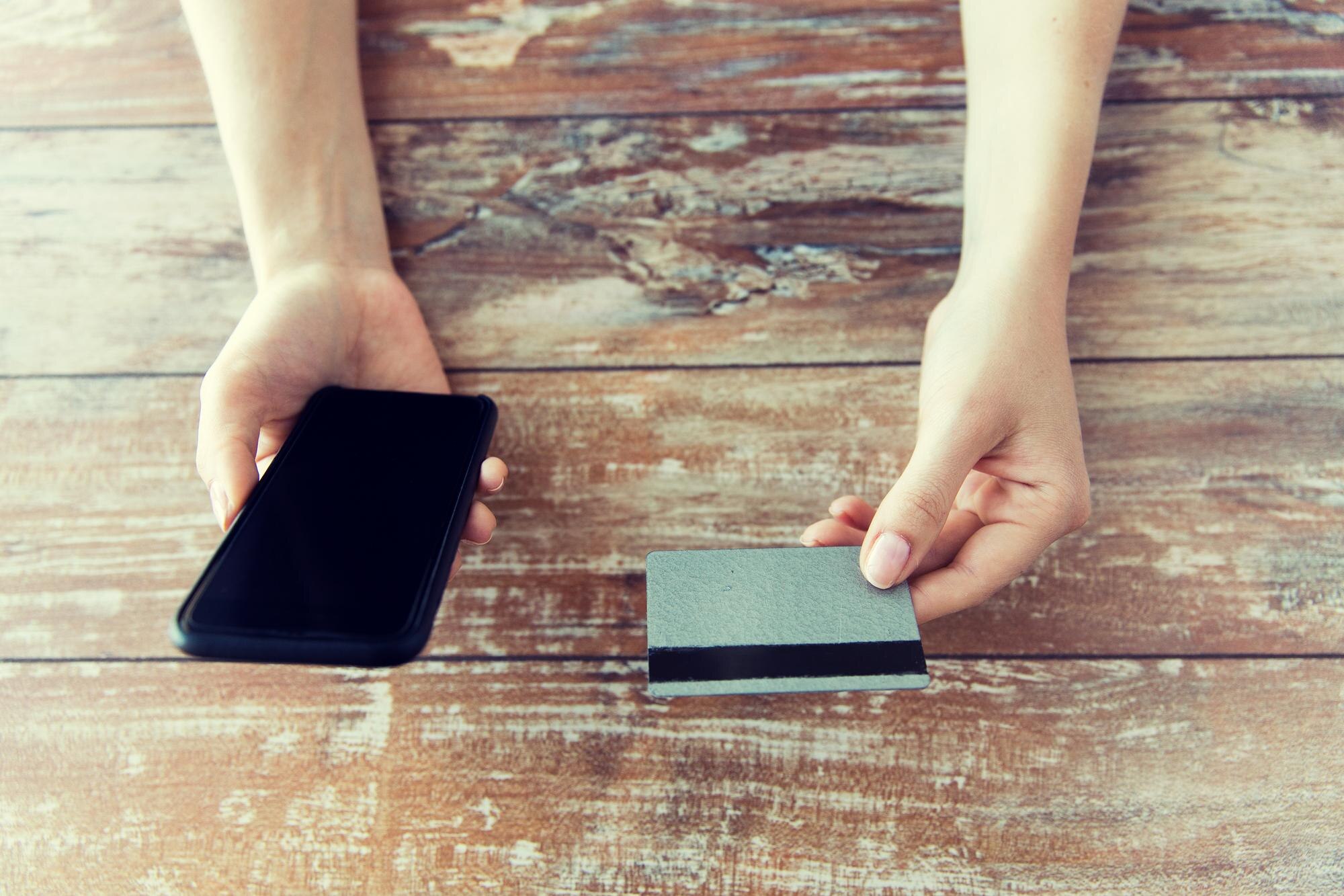 koncepcja biznesu, technologii, gotówki i Internetu - zbliżenie męskich rąk trzymających inteligentny telefon i kartę kredytową na drewnianym stole