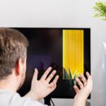 Frustrated person with hands reacting to a severely broken computer monitor displaying colorful lines signifying technical damage repair and unexpected expense
