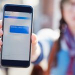 Hand phone screen and cyber bullying at college with text message stalker or notification at campus Person smartphone and rude chat with harassment mobile app and social network at university