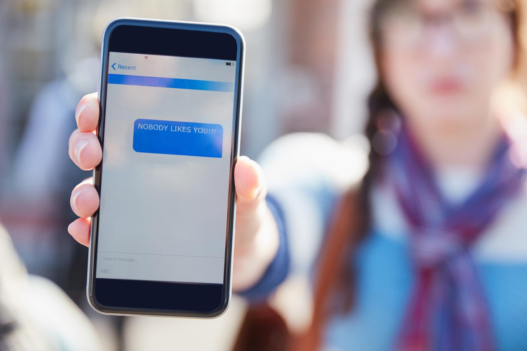 Hand phone screen and cyber bullying at college with text message stalker or notification at campus Person smartphone and rude chat with harassment mobile app and social network at university