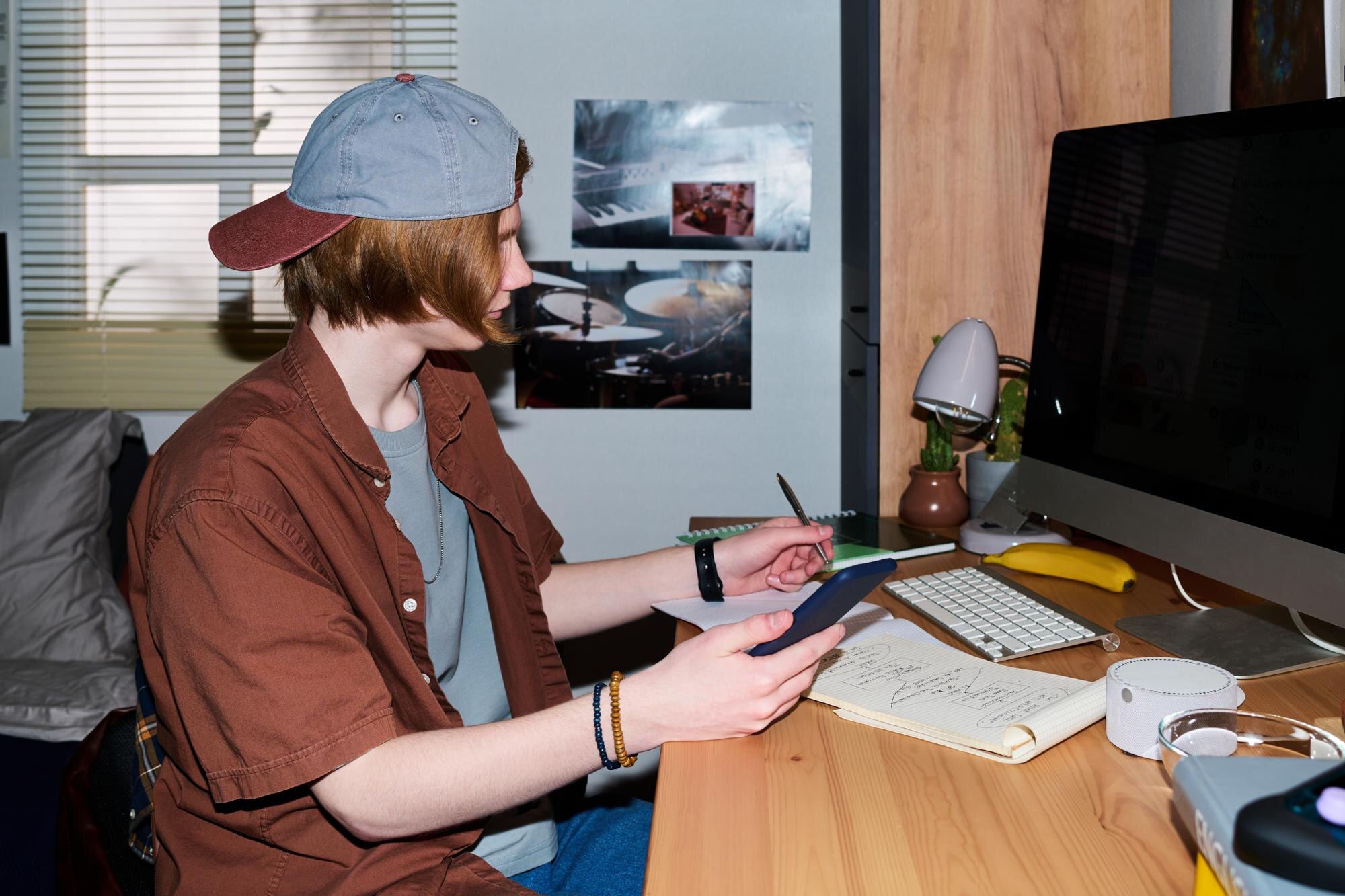 Teenage boy using tablet and taking notes at home desk