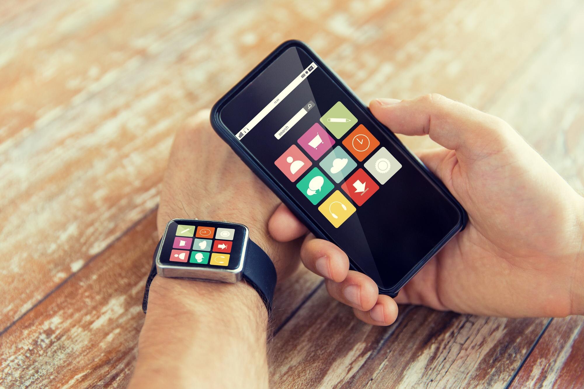 nowoczesna technologia, aplikacja i koncepcja ludzi - zbliżenie męskiej dłoni trzymającej smartfon i noszącej zegarek z ikonami aplikacji na ekranie w domu