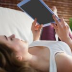 Ładna kobieta, leżąc na kanapie podczas korzystania z tabletu w salonie