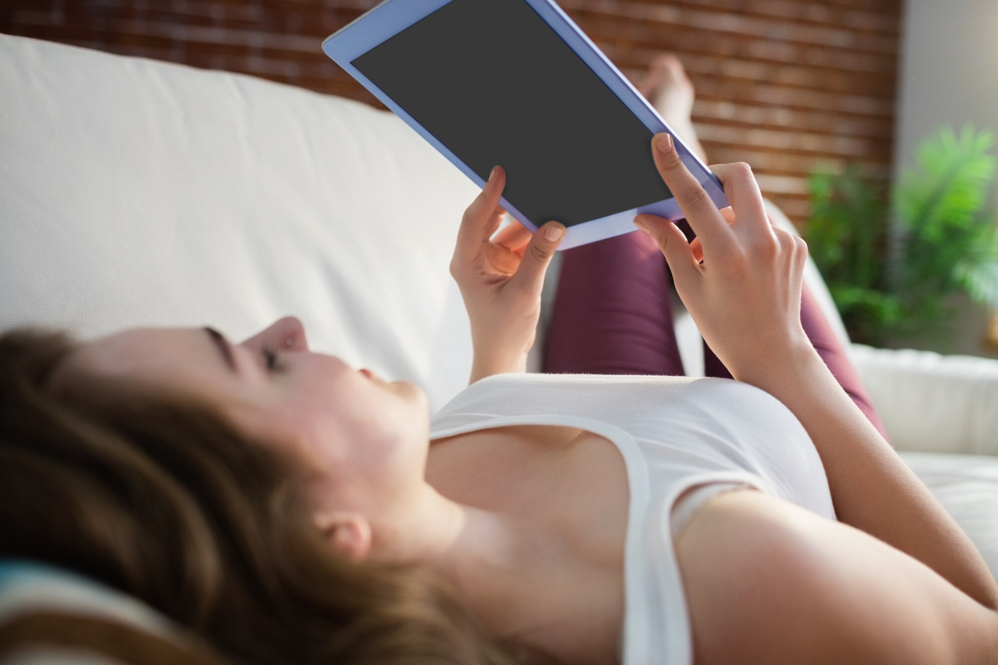 Ładna kobieta, leżąc na kanapie podczas korzystania z tabletu w salonie
