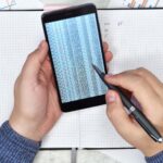 Ręce księgowego za pomocą telefonu komórkowego z raportem finansowym