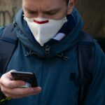 Facet w masce ochronnej na ulicy używa smartfona