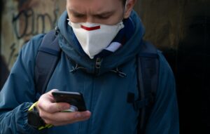 Facet w masce ochronnej na ulicy używa smartfona