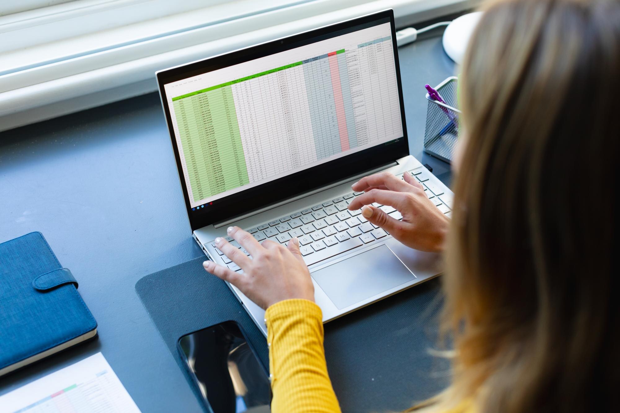 Biała kobieta siedząca przy biurku, pracująca z domu i używająca laptopa w słonecznym pokoju