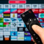 Inteligentna domowa ręka trzymająca pilota zdalnego sterowania z aplikacjami z inteligentnego telewizora na tle