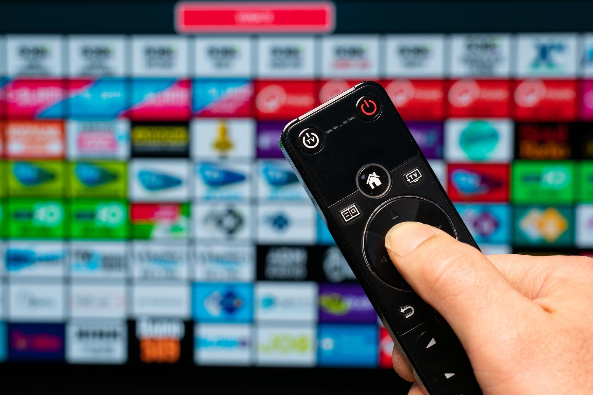 Inteligentna domowa ręka trzymająca pilota zdalnego sterowania z aplikacjami z inteligentnego telewizora na tle